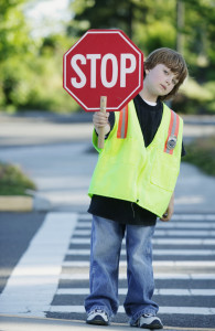 Portrait of a young boy crossing guard standing on the road holding a stop sign